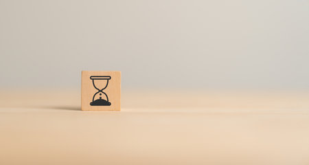 Time management concept. Self-discipline, organization, and prioritizing tasks. Project timeline and due date. Wooden cube block with hourglass icon on grey background and copy space.の写真素材