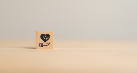 Health insurance concept. Healthcare, finance and medical service. Wooden cube block with hand holds heart pulse, heartbeat lone and cardiogram symbol. Healthcare, medical background and copy space.の写真素材