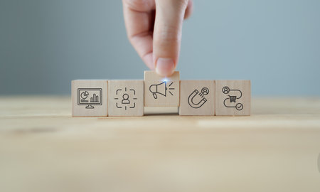 Marketing strategy planning with wooden blocks. A hand arranging wooden blocks with  icons representing data analytics, customer targeting, advertising, lead generation and sales process.の写真素材