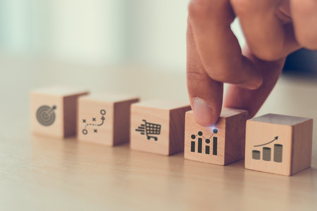 Sales strategy and performance concept. A hand arranging wooden blocks with icons symbolizing sales target, data analytics, strategic planning, sales team management and sales performance.の写真素材