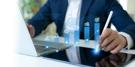 Business growth strategy concept. A professional uses a digital tablet to interact with blue bar graphs and business strategies icons; teamwork, innovation, business collaboration, sustainability.の写真素材