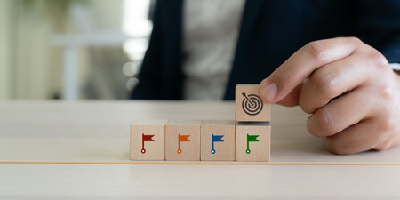 Goal setting and achievement concept. Step by step success strategy. Wooden blocks with flag and target icon. Progress tracking, goal setting and achievement in business or personal development.の写真素材