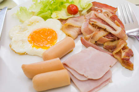 Breakfast style ham bacon and sausage with egg on white plateの写真素材