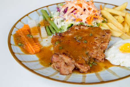 Pork steak with vegetables and potato in dish on white backgroundの写真素材