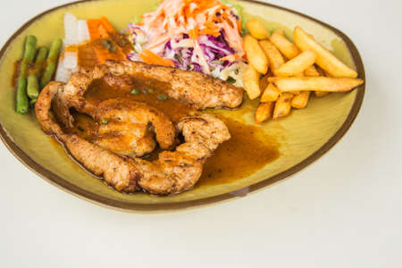 Chicken steak with vegetables and potato in dish on white backgroundの写真素材