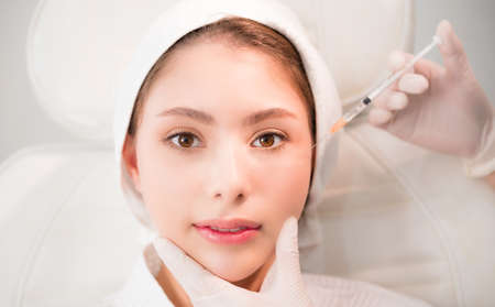 Beauty clinic concept. Asian woman lying on bed and cosmetologist does injections to face augmentation for anti wrinkle in beauty clinic. Young women getting anti aging injection in surgery clinic.の写真素材