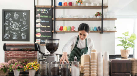 Asian girl startup small business of coffee shop concept. Beautiful female barista standing behind bar counter in cafe. Happy young barista woman wearing aprons and check customer order for delivery.の写真素材