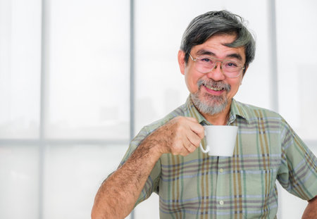 Happy senior asian man sitting on couch and holding coffee cup ready to drink in living room....