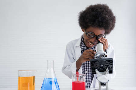 African american child boy student is learning and test science chemical by looking to microscope in laboratory room at to school. Education and science research concept.の写真素材