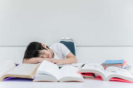 Asian boy wear glasses is tired from reading and sleeping on stack book. Child learning from home and quarantine while outbreak of disease from coronavirus or covid-19. New normal education concept.の写真素材