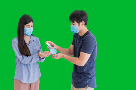 Asian couple standing wear hygiene mask and using alcohol gel or sanitizer for cleaning hands to protective infection and outbreak of coronavirus or covid-19 isolated on green background. New normal.の写真素材