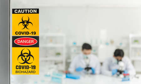 Team of medical researcher are testing vaccine from plasma of blood for protect coronavirus or covid-19 in biohazard laboratory. Caution symbol and biohazard symbol to stick on glass in front of lab.の写真素材