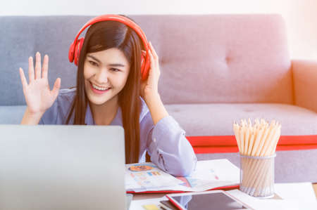 Beautiful asian businesswoman working at home. Young female sitting and wear red headphone with...