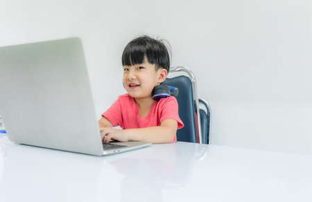Happy child boy wear headphone and enjoy listening music by laptop computer with sitting on chair in...