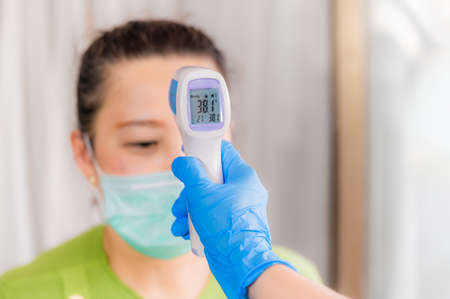 Asian doctor using infrared forehead thermometer gun checking of woman wear mask to assess status...