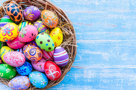 Beautiful colorful easter eggs in wicker basket on blue table wooden with vintage style.