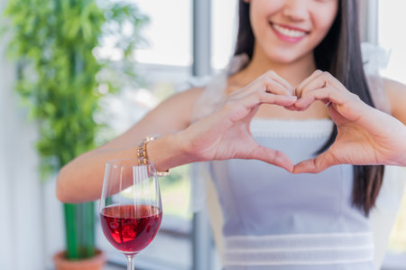 Beautiful asian young woman sitting and happy smiling with showing heart sign shaped by her hands in restaurant. Valentine's day concept.の写真素材