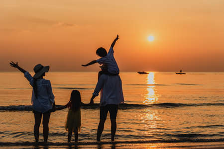 Happy asian family at consisting father, mother, son and daughter having fun on summer vacation on the beach with sunset. Family holiday travel concept.の写真素材