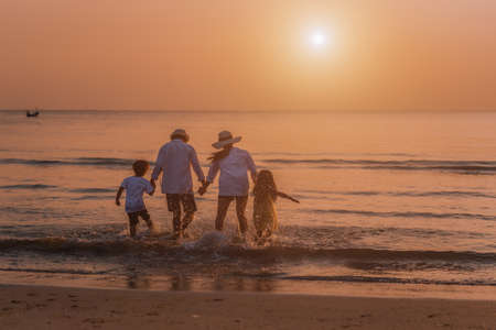 Happy asian family at consisting father, mother, son and daughter having fun on summer vacation on the beach with sunset. Family holiday travel concept.の写真素材