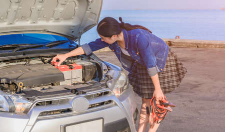 Beautiful asian young woman holding battery cable charge for car. Automotive motor problem and...