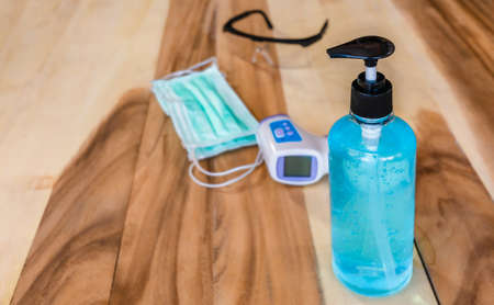 Preliminary personal protective equipment for prevention corona virus or covid-19. Alcohol gel or sanitizer, surgical mask or protection mask, safety goggles and infrared thermometer on wooden table backgroundの写真素材
