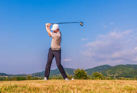 Asian golfer hitting golf ball on green fairway with driver from teebox on mountain and blue sky background.の写真素材