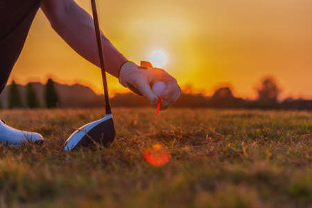 Close up of golfer hand holding golf ball and golf tee with driver on sunset background.の写真素材