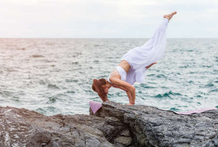 Asian woman is practicing yoga on the asana in outdoors with sea and sky background. Healthcare and exercise concept.の写真素材