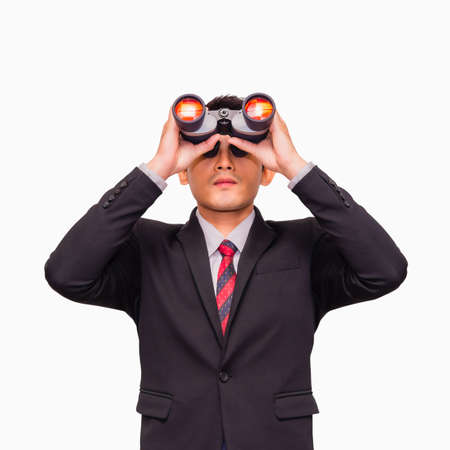 Asian young businessman standing and looking through binoculars isolated on white background. Business and looking for the new opportunities concept.の写真素材