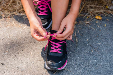 Closeup of woman athlete tying laces of shoes for jogging at roadside on outdoor. Healthy and lifestyle concept.の写真素材
