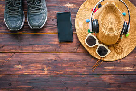 Top view of accessories to summer beach consisting of straw hat, sunglasses, smartphone, sneakers with headphone on the old wooden table. Summer holiday concept.の写真素材
