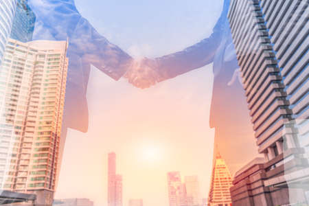 Double exposure of businessman standing handshake on outdoors with city background. Business partnership and teamwork concept.の写真素材