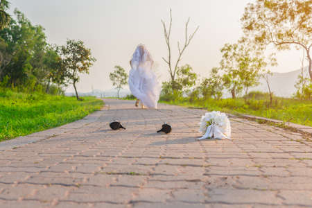 Beautiful bride wearing a white wedding dress running away alone in nature outdoor with leaving a...