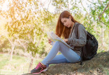 Portrait beautiful female travelers sitting on tree roots with checking map in the forest. Woman...