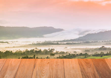 Empty top of wooden table and view of sunrise forest nature with the mountain and mist landscape.の写真素材