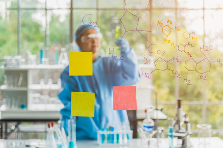 Asian woman science specialist laboratory working at lab to checking test tubes with chemical equations and use  notes to share idea. Laboratory science concept.の写真素材