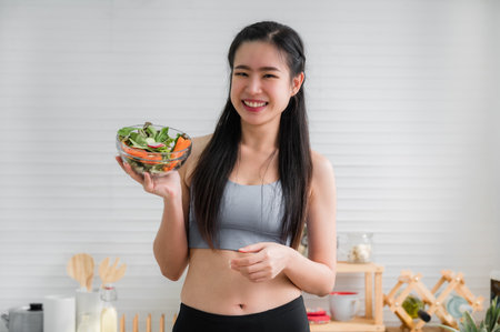 Portrait of healthy woman in sportswear stand smile and holding salad bowl in kitchen at home. Happy...