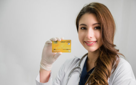 Portrait of happy beautiful Asian woman doctor in white gown with stethoscope standing hold credit card in office at hospital. Young Female medical smile with show card for health insurance in clinic.の写真素材