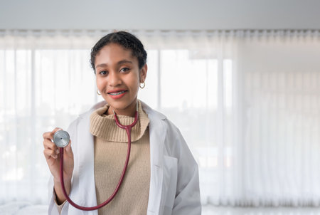Portrait of happy African woman professional doctor in uniform standing holding stethoscope and look at camera in white room at hospital. Black female medical wear braces on teeth and smile in clinic.の写真素材