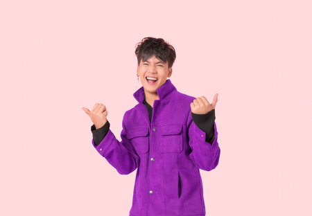 Portrait of happy Asian handsome young man in fashionable jacket clothes standing smiling with thumbs up and look at camera isolated on pink background. Attractive male model lifestyle face gesture.の写真素材