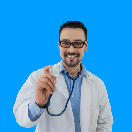 Portrait of happy Asian handsome man medical doctor in uniform wearing glasses standing smiling holding a stethoscope and looking at camera isolated on blue background. Healthcare and service concept.の写真素材
