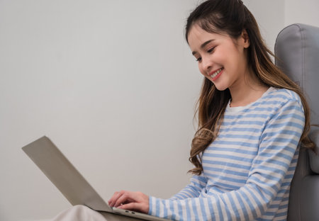 Portrait of happy Asian young woman sitting smiling and using laptop computer for shopping online with cheerful and enjoying in living room at home. Pretty female student learning online by notebook.の写真素材