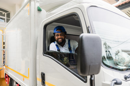 Happy African American delivery service man driver in uniform sitting smiling and looking on camera cheerful in a courier truck. Concept of industry business shipping and moving.の写真素材