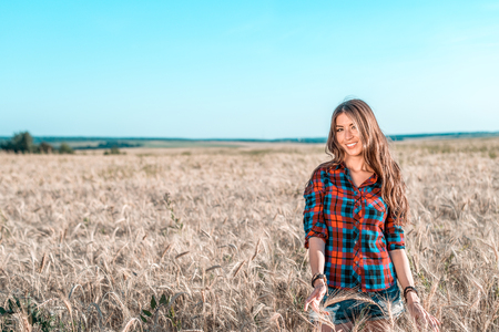 Beautiful happy girl in the field, sunny afternoon, shorts shirt. The concept of enjoying nature. Rest on the air. Walking through the meadows in wheat in the summer.の写真素材