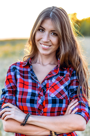 Beautiful girl in the field. Summer in nature. Happy smiling looking in frame. In the evening shirt a brunette woman, a close-up portrait, a concept of fun. Close-up portrait.の写真素材