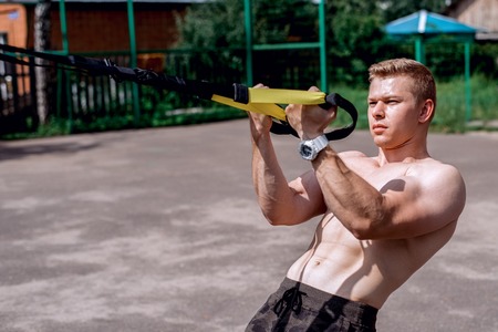 A male athlete is engaged in an open air loop, coaches a bicep fence. In summer, in shorts and a bare torso. Healthy lifestyle of young people. The concept of sport motivation.の写真素材