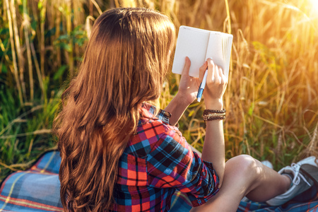 Beautiful happy girl in the field, sunny day shirt. Concept new ideas, writing in notebook. enjoyment of nature. Rest on the air.の写真素材
