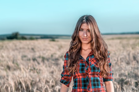 Beautiful girl in the field. Summer in nature. Corrects long hair. In a shirt and shorts. A sunny day woman brunette, close-up portrait.の写真素材