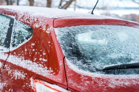 Rear window of the car. Close-up of a red window machine covered with snow. Winter in the city. The car is in the parking lot in the winter.の写真素材
