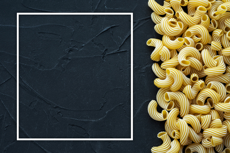 Raw cavatappi Beautiful decomposed pasta with the right, on its side on a black textured background. Close-up view from the top. Free space for text. With white frame for text.の写真素材